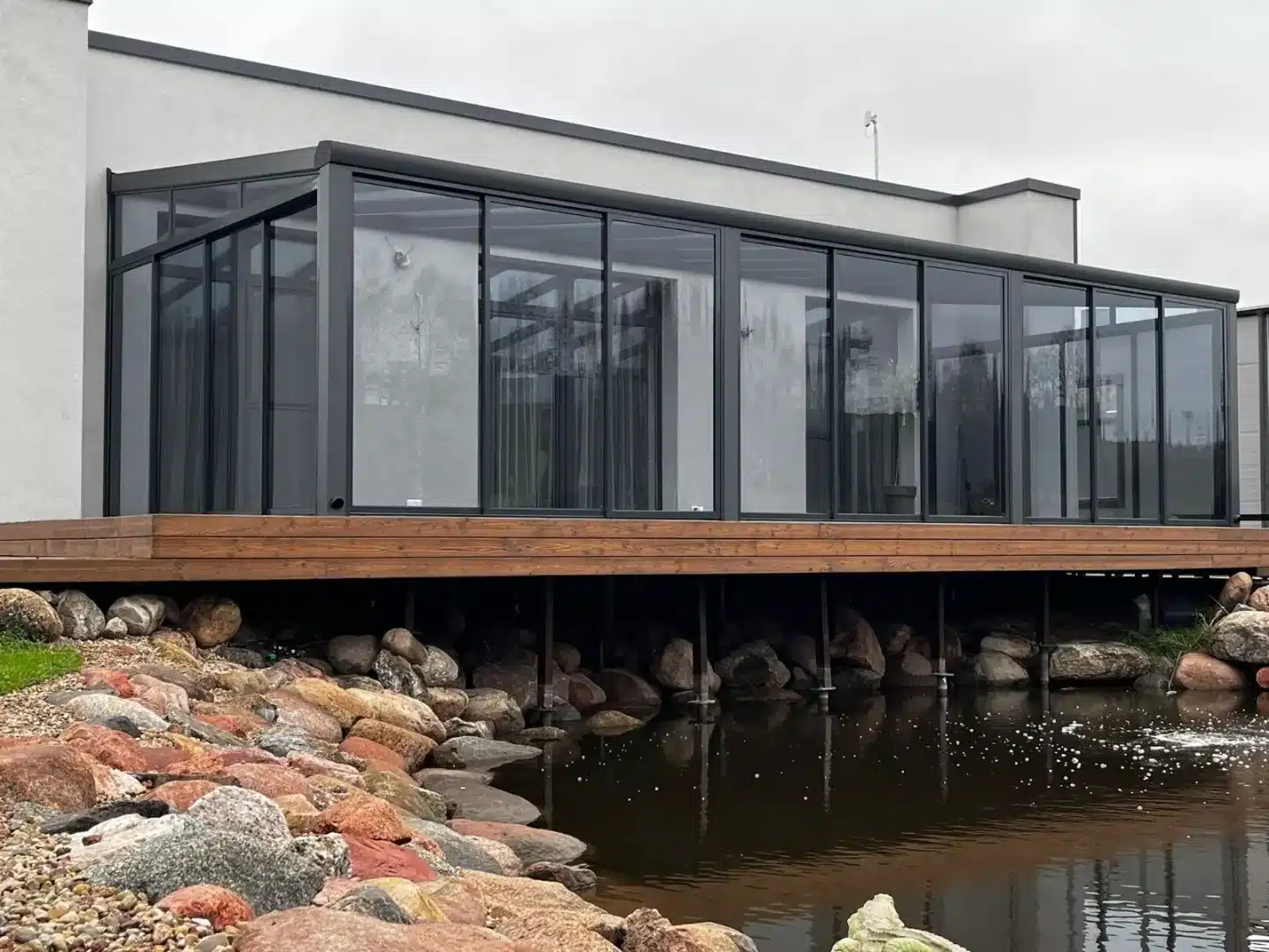Glass roof extension with sliding doors beside a pond
